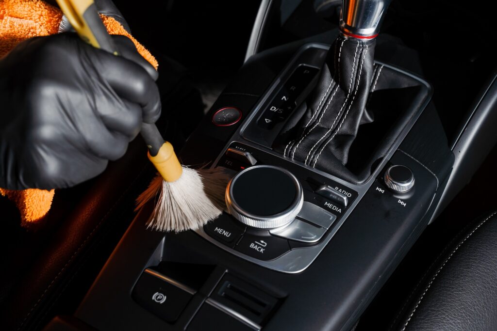 Dry cleaning with brush of gearbox and dashboard in car. Auto interior specialty detailing service. Cleaning individual elements of black leather interior in auto.